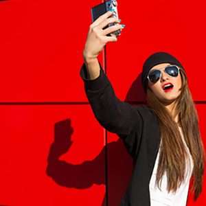 Trendy girl taking selfie against red wall